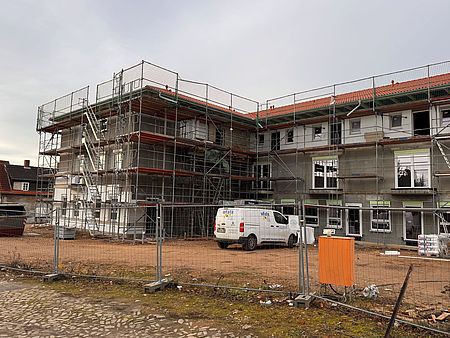 Tag der offenen Baustelle Ambulantes Quartiershaus Ein Quartiershaus wird von einem Baugerüst umgeben. Das Gebäude ist teilweise verdeckt, während Bauarbeiten stattfinden. Rundherum sind Materialien und Geräte einer Baustelle zu sehen.