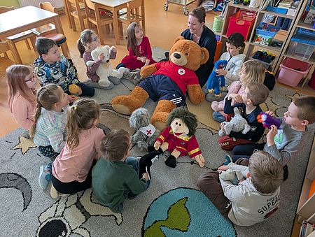 Henry und Mischi in der Kita Hohendodeleben Mehrere Kindergartenkinder sitzen im Kreis um drei Stoffpuppen.