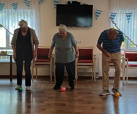 Die Gäste der Tagespflege vergnügten sich beim Kartoffelfest mit Spielen rund um die Knolle. 3 Senioren stehen nebeneinander und schaue herunter zu einer Kartoffel vor ihren Füßen