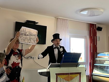 Literarisch-musikalischer Nachmittag in Osterweddingen Ein Mann in Frack und Zylinder steht an einem Keyboard. Eine Frau daneben hällt eine Zeichnung hoch