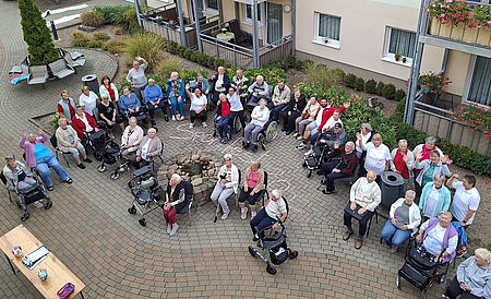 Die Teilnehmer und Helfer des Sportfests am Rot-Kreuz-Zentrum „Obere Aller" in Eilsleben. Circa 30 Seniorinnen und Senioren, teils in Rollstühlen oder mit Rollatoren winken in die Kamera, die aus dem 2. Stockwerk nach unten fotografiert