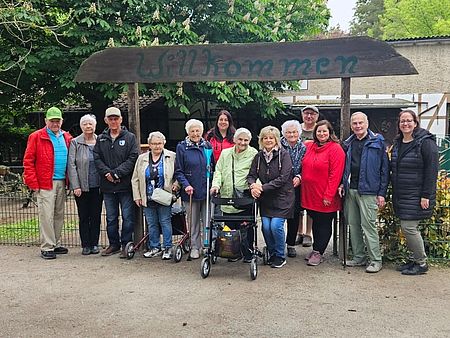 Die Tagespflege Osterweddingen zu Besuch im Staßfurter Zoo Eine Gruppe Senioren und BEtreuer stehen unter einem hölzernen Wilkommenschild