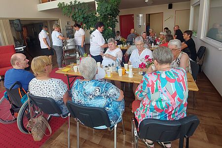 Sommerfest in der Begegnungsstätte in Eilsleben Senioren sitzen an mehreren Tischen. Becher mit Bowle stehen auf den Tischen. Im Hintergrund wir gegrilltes ausgegeben
