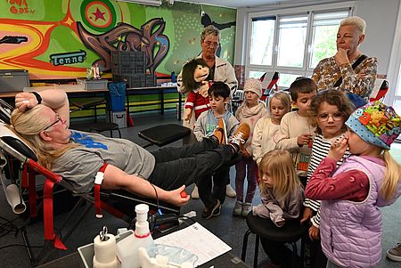 Kinder der Kita Wanzleben besuchen die Blutspende Mehrere Kinder und zwei Hortnerinnen stehen neben einer Liege, auf der eine Person liegt und Blutspendet